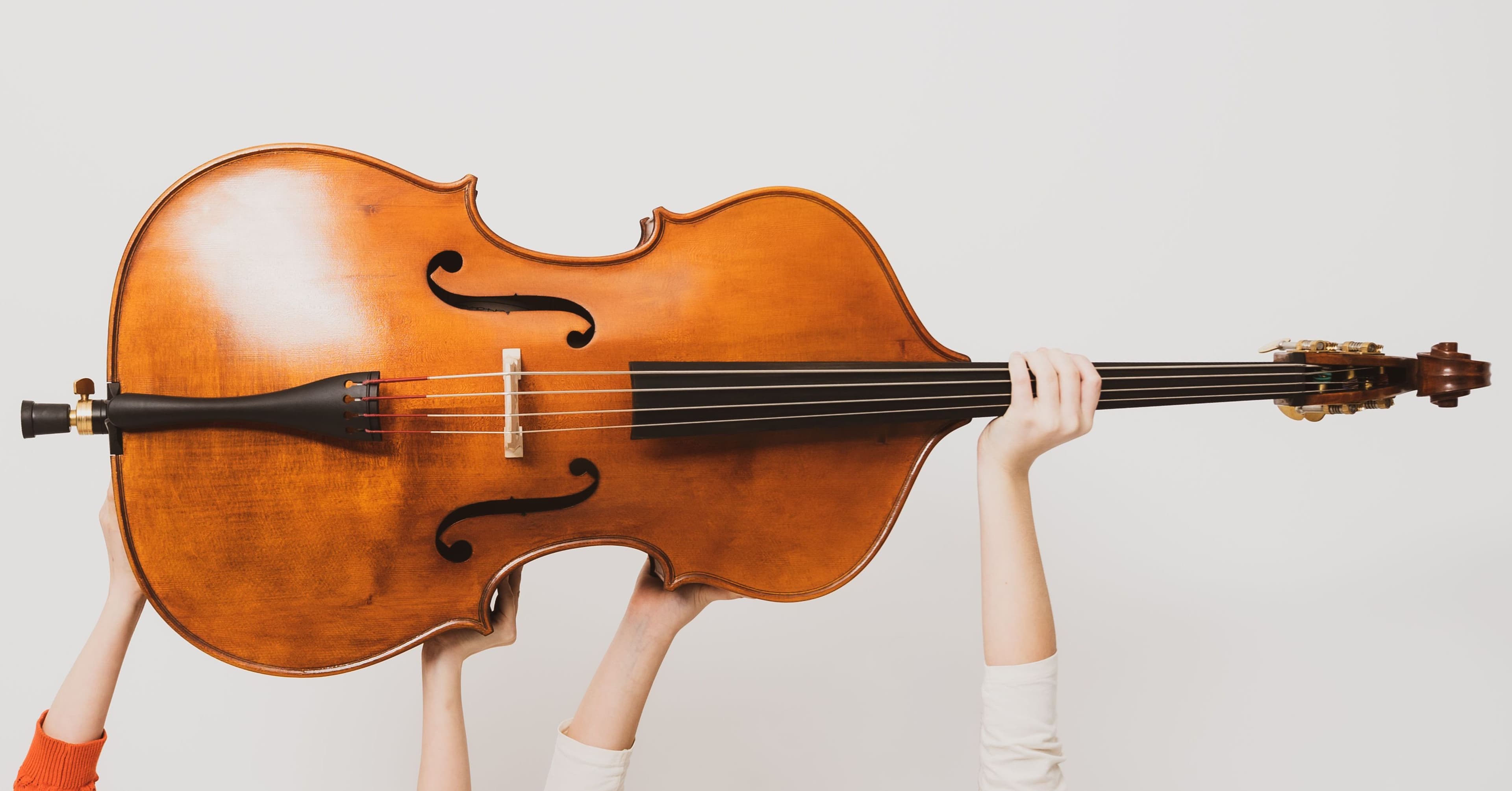 Zwei Kinder, die nicht zu sehen sind, halten mit beiden Armen einen Kontrabass hoch.