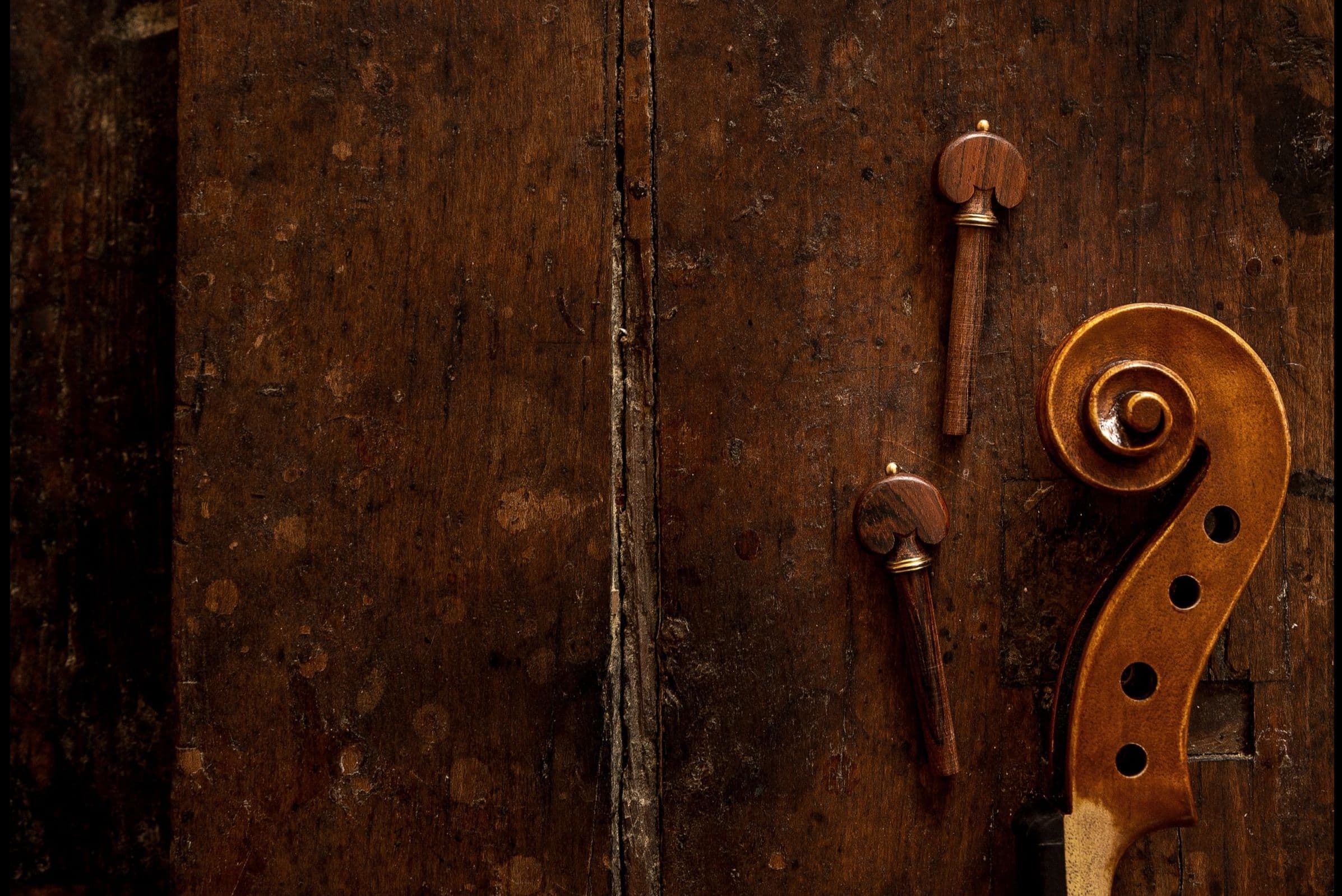 Auf einer Werkbank liegen rechts zwei Geigenwirbel und die Schnecke einer Geige.
