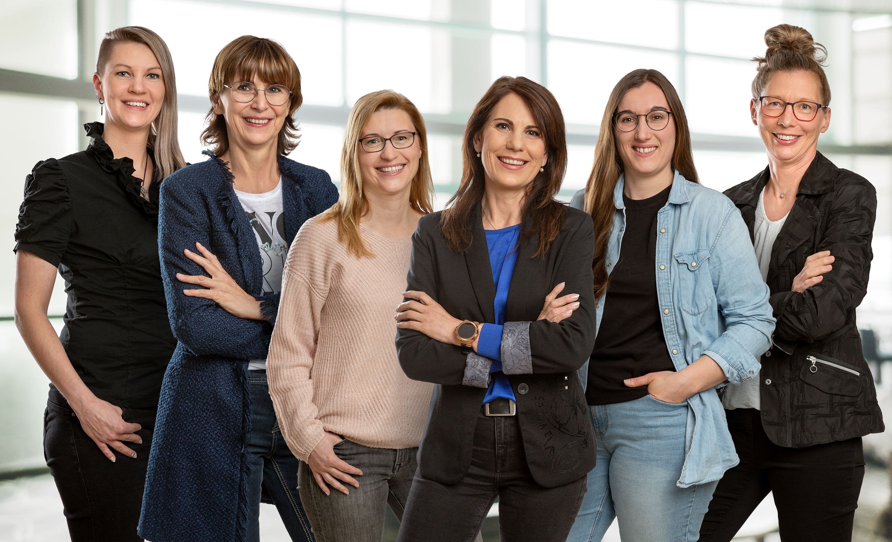 unsere sechs Büromitarbeiterinnen stehen nebeneinander und lächeln freundlich