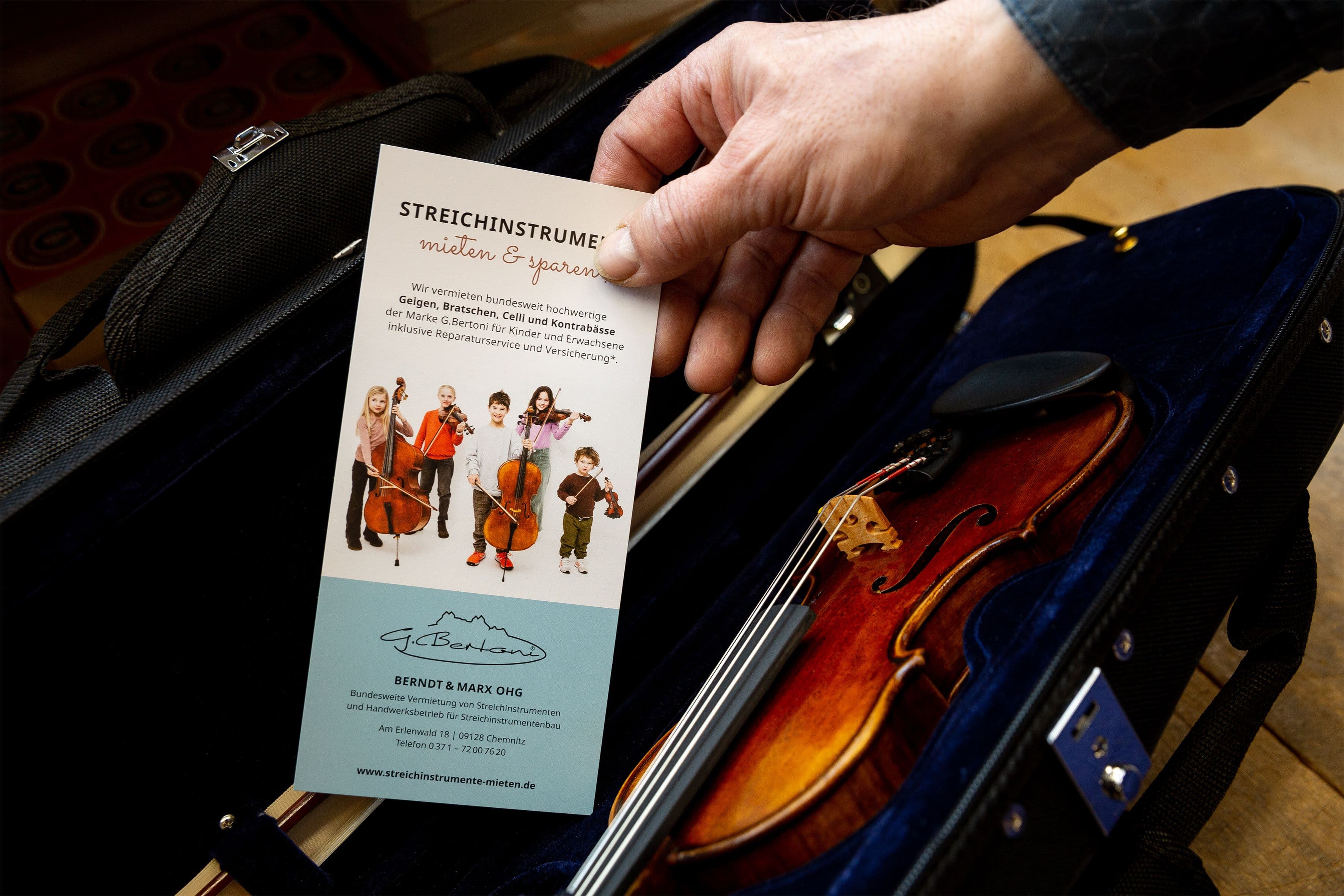 Über einem geöffneten Geigenetui hält jemand hält einen Werbeflyer in der Hand.