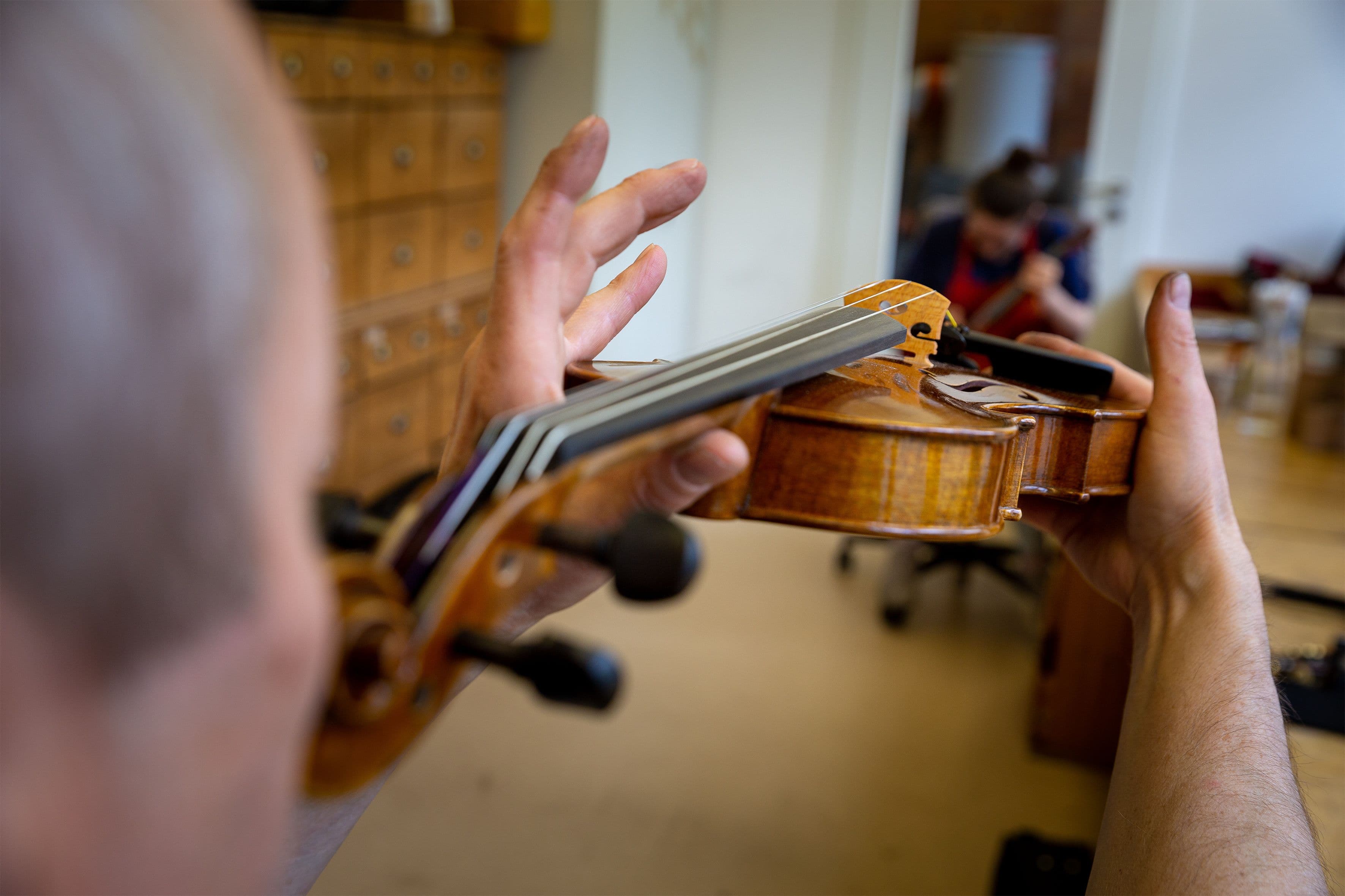 Ein Werkstattmitarbeiter prüft die Saitenlage einer Geige.